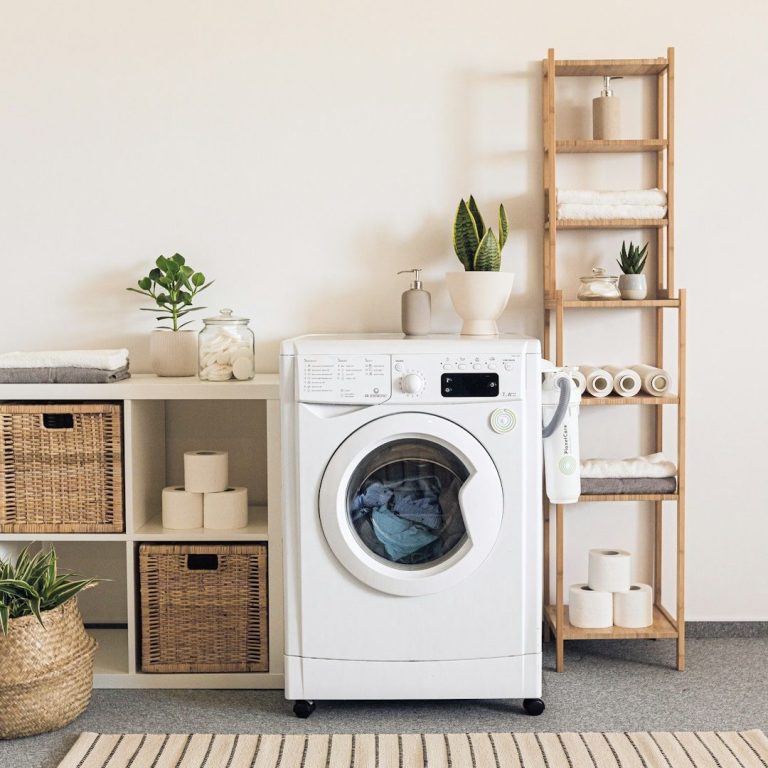 Lave-linge blanc à côté d'une étagère en bois, plantes et paniers en osier.